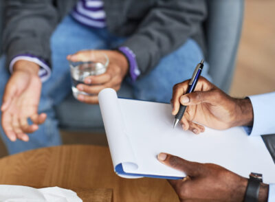 Adolescent psychologist taking notes when discussing problems with teenage boy
