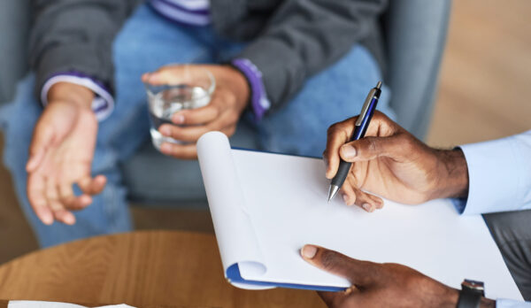 Adolescent psychologist taking notes when discussing problems with teenage boy